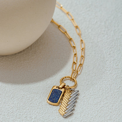 Flat-lay shot of dual-tone pendant necklace with rectangular lapis charm and metallic feather