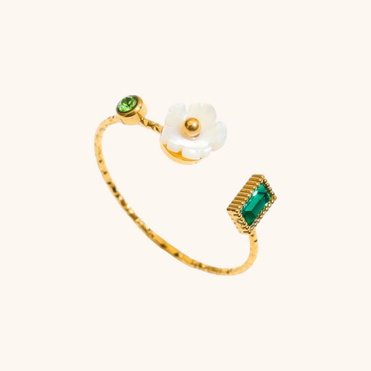 Gold open ring with white flower and green crystal on white plate
