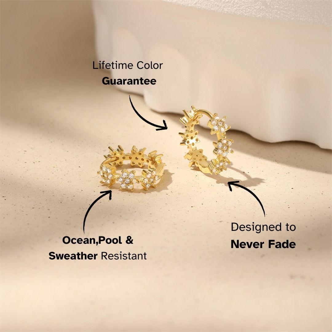 Gold floral sparkle huggie earrings on beige background with shadow, designed for waterproof wear