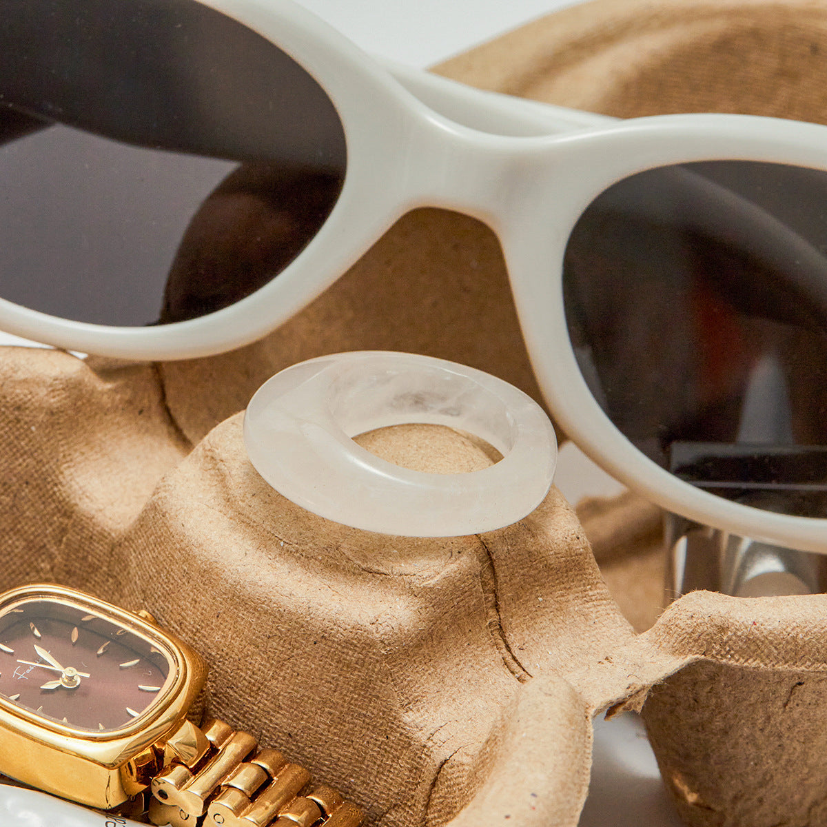 White frosted resin ring with smooth finish shown next to gold watch and sunglasses.