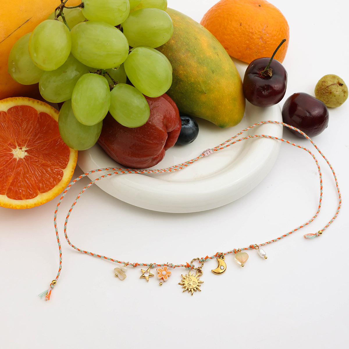 Orange and white braided cord necklace with celestial charms displayed next to tropical fruits