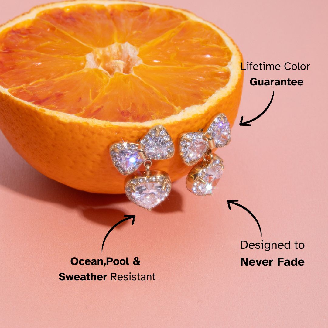 Gold bow and heart crystal earrings displayed on orange fruit, waterproof and tarnish-free