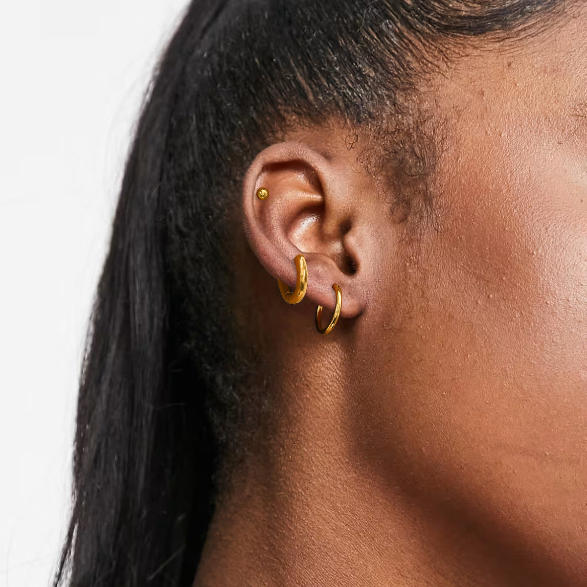 Woman wearing gold stud and hoop earrings, layered ear styling for everyday fashion