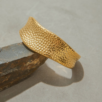 Modern gold bangle bracelet placed on a stone slab, showcasing its shine and textured finish