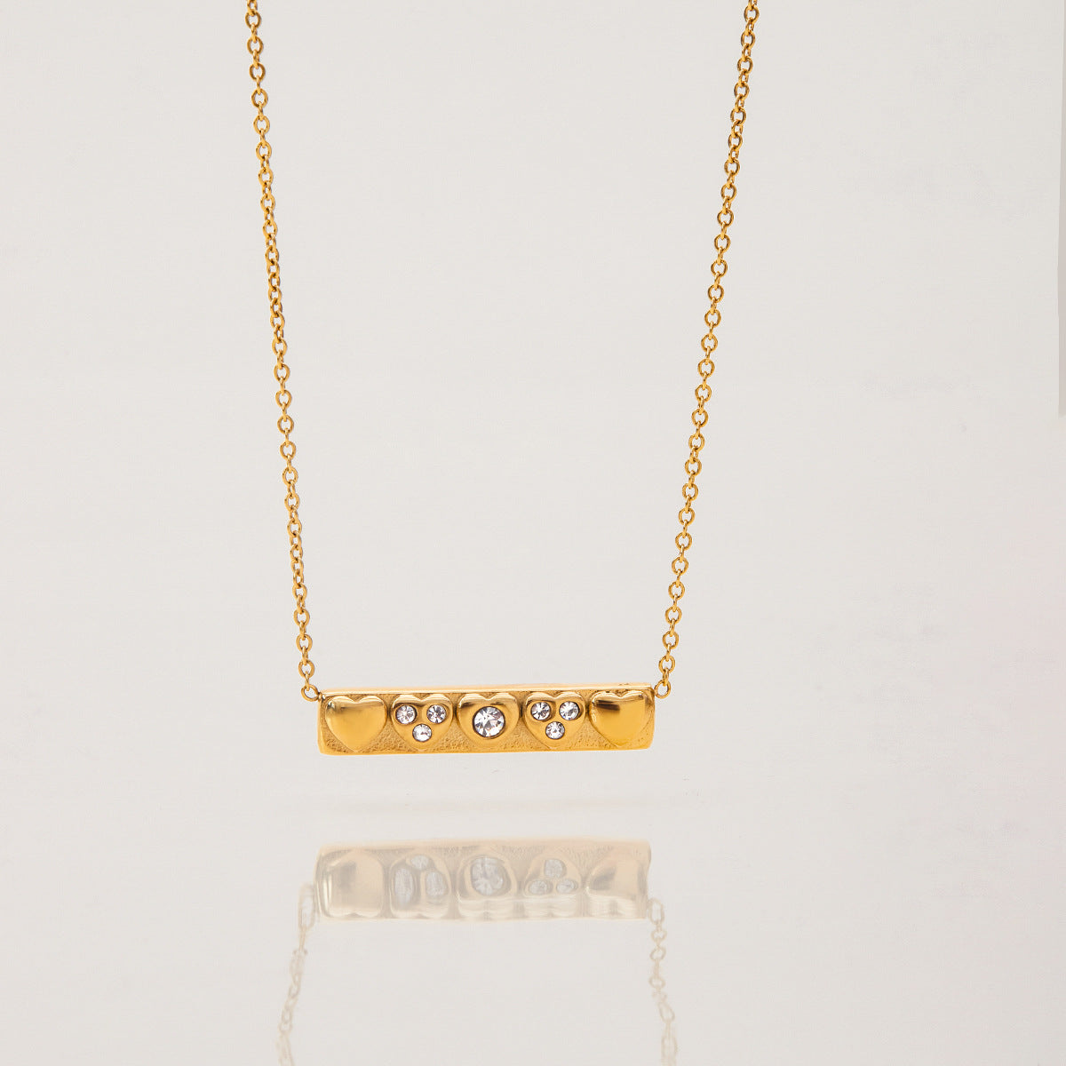 Minimalist bar necklace with engraved hearts and sparkling stones, laid flat