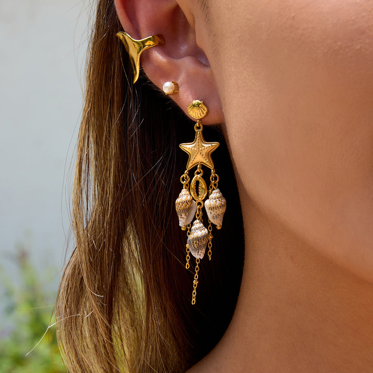 Model wearing gold starfish shell earrings in summer sunlight