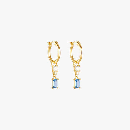 A pair of gold hoop earrings with a blue gemstone and diamond drop.