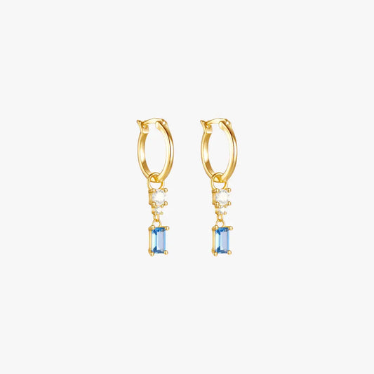 A pair of gold hoop earrings with a blue gemstone and diamond drop.