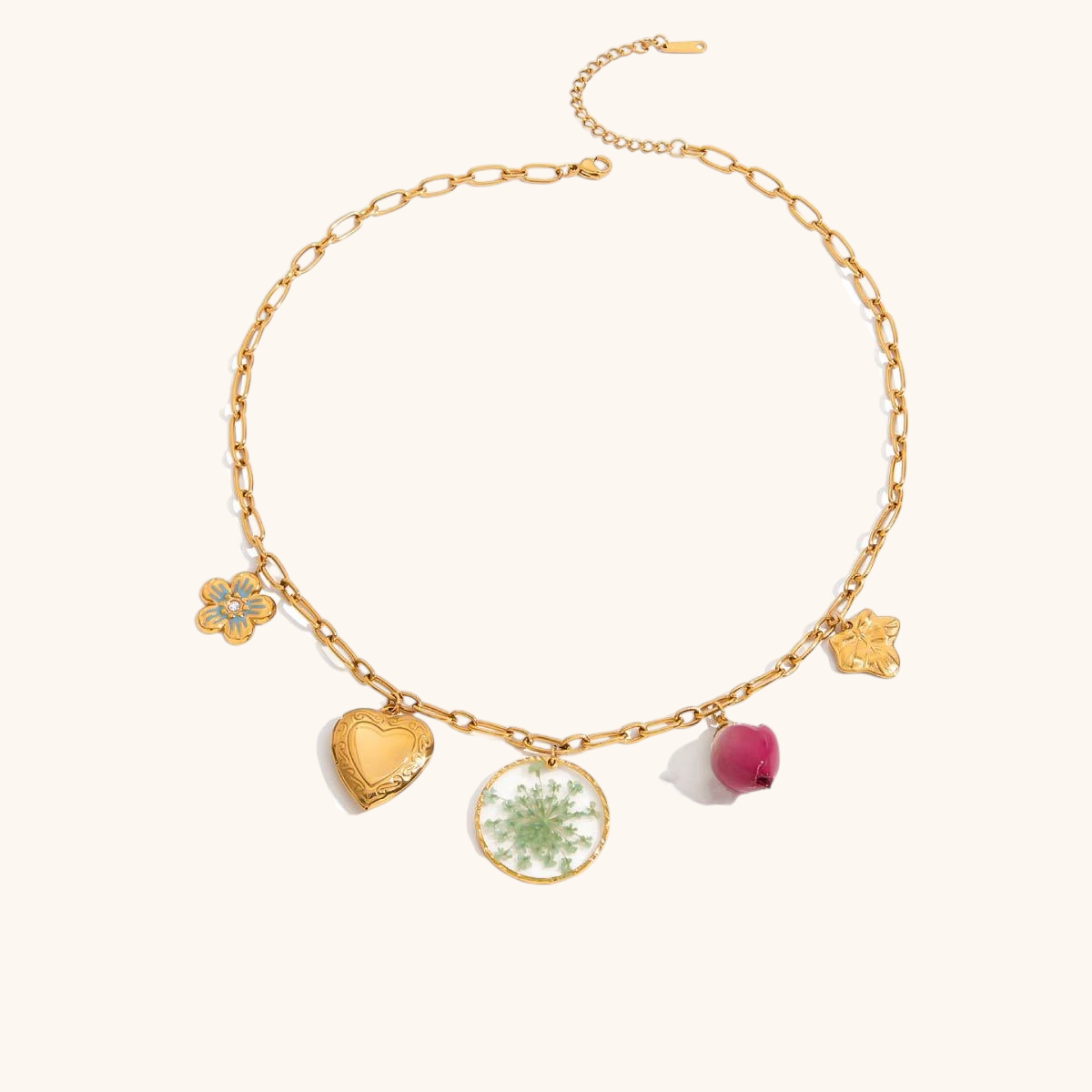 Studio shot of gold charm necklace with green resin flower disc, heart locket, and dried rosebud