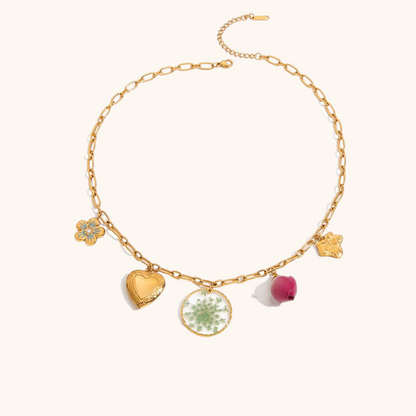 Studio shot of gold charm necklace with green resin flower disc, heart locket, and dried rosebud