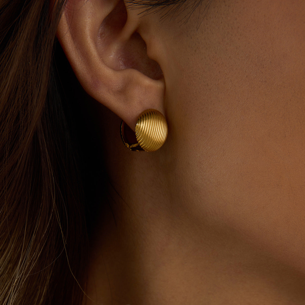 Close-up of model wearing ribbed gold dome clip-on earrings, showing elegant fit on earlobe