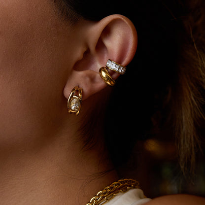 Woman wearing gold sculpted crystal studs with stacked ear cuffs in a warm-lit scene
