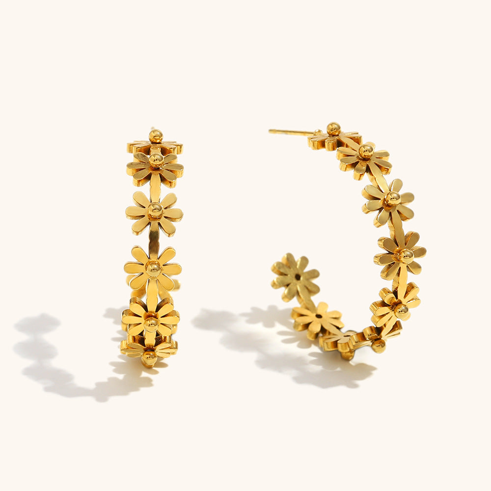 gold flower hoop earrings with daisy petals, laid flat on neutral surface with soft shadows