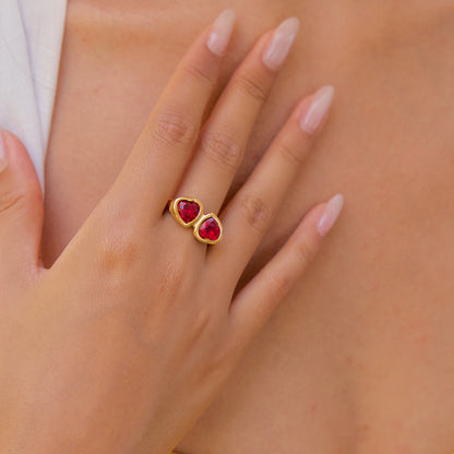 Woman’s hand wearing a gold double-heart gemstone ring in daylight