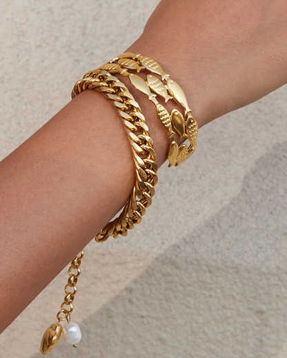Gold bracelet with leaf design on a wrist against a neutral background