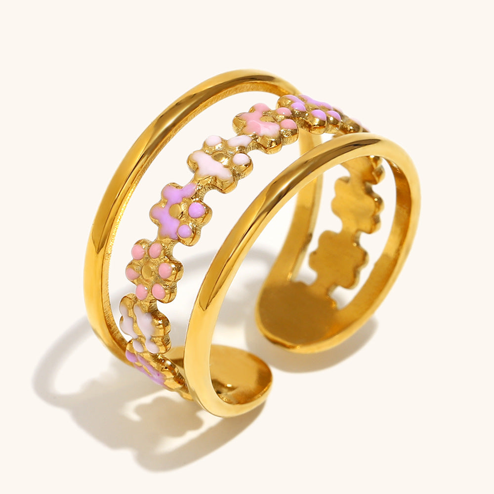 Adjustable gold ring featuring pink enamel flower details, captured on sandy backdrop.