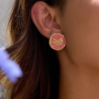 Model wearing gold butterfly stud earrings with pink enamel swirl