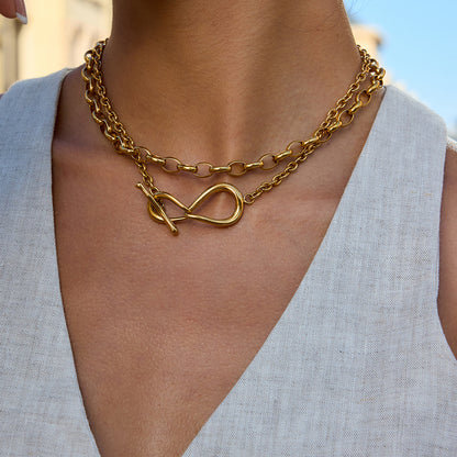 Gold chain necklace with a unique clasp design worn by a person against a neutral background