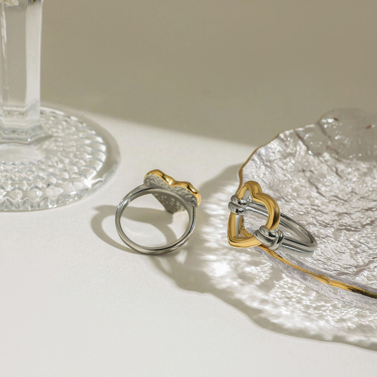 Two-tone heart rings with modern design near clear dish in daylight