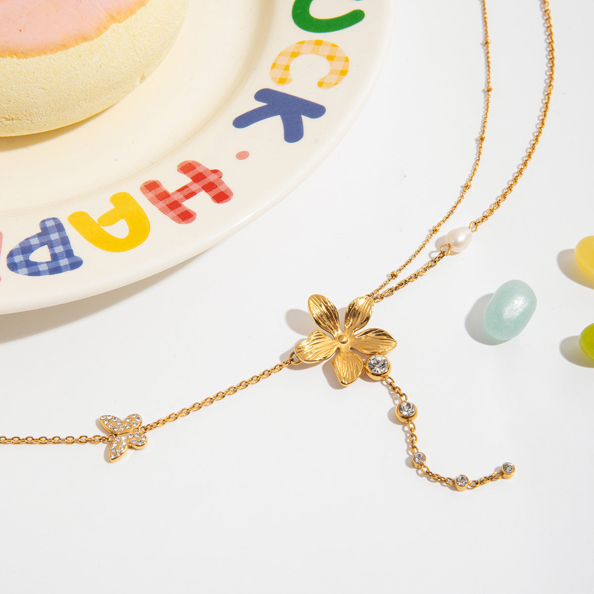 Gold necklace with floral design on a white surface with colorful letters in the background