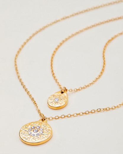Two gold necklaces with circular pendants on a light gray background