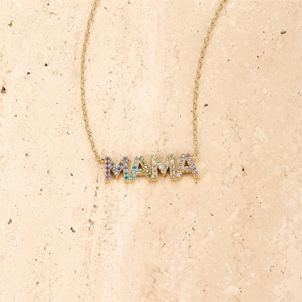 Close-up of rainbow zircon MAMA necklace with gold chain on textured background.