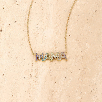 Close-up of rainbow zircon MAMA necklace with gold chain on textured background.