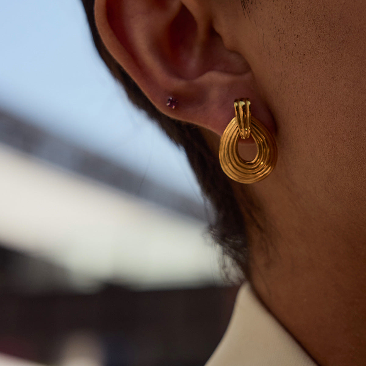 Female model wearing bold gold layered teardrop earrings outdoors