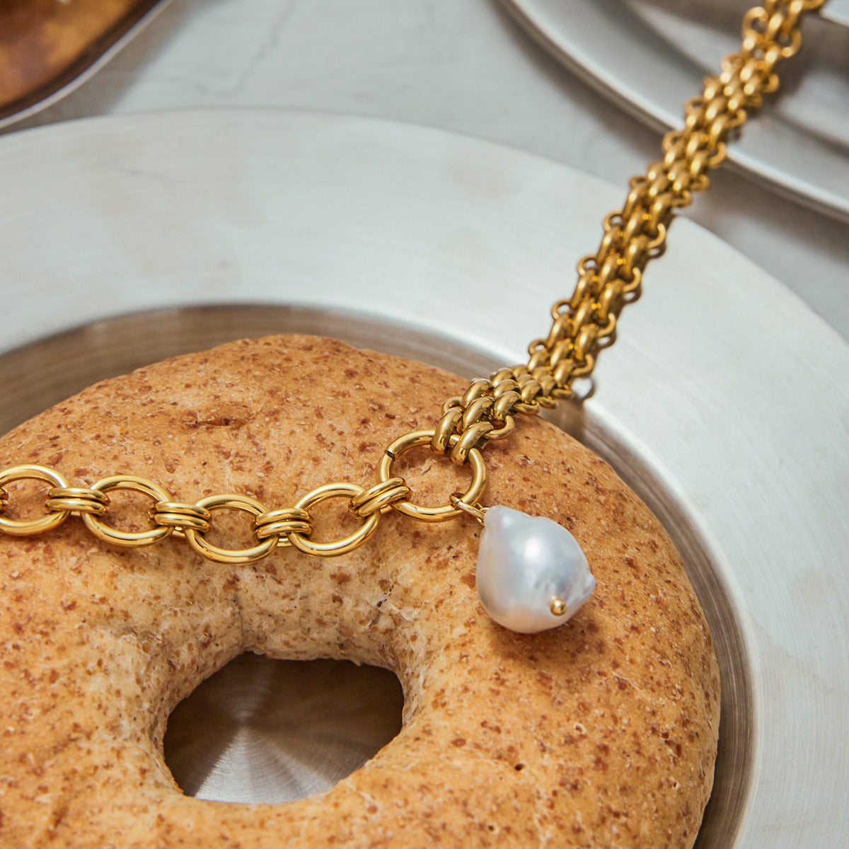 Close-up of chunky link necklace with teardrop pearl, styled with soft bread tones