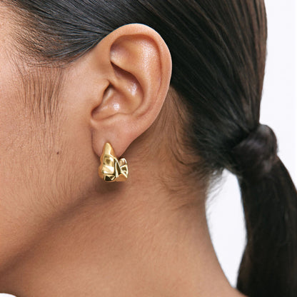 Woman wearing abstract gold sculpted hoop earrings with hair tied back