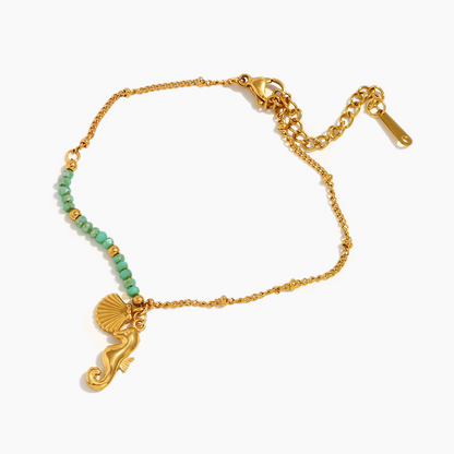 Gold bracelet with green beads and a seahorse charm on a white background