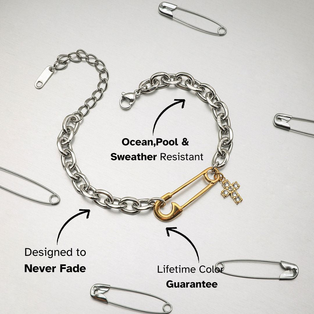 Stylish two-tone bracelet with gold safety pin and rhinestone cross, laid flat on a silver background.