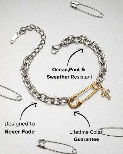 Stylish two-tone bracelet with gold safety pin and rhinestone cross, laid flat on a silver background.