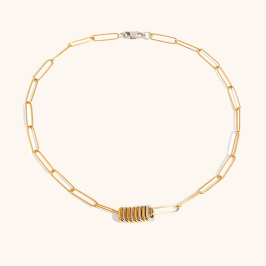 Stylish gold chain necklace with stacked silver and gold discs, shown in a clean product image on a beige backdrop.