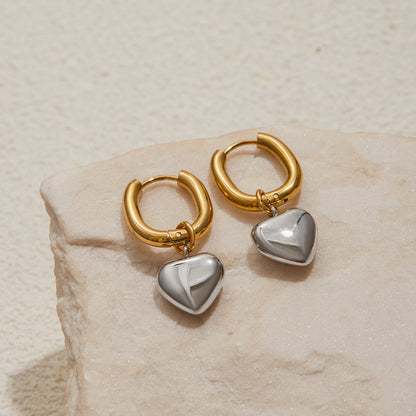 Gold hoop earrings with heart-shaped charms on a beige stone surface