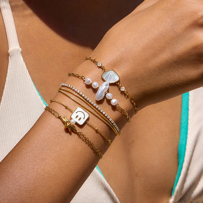 Close-up of a woman's arm wearing multiple gold bracelets with pearls and charms.