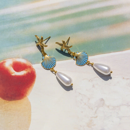 Gold starfish earrings with blue shell charms and pearl drops on textured backdrop
