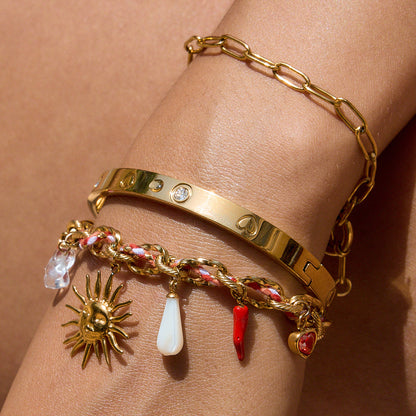 Gold bracelet with various charms on a wrist against a neutral background