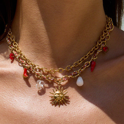 Gold chain necklace with sun charm and red and clear beads on a person's neck.