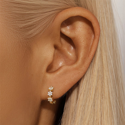 Petite gold huggie earrings with flower-shaped zircon stones on a soft ear