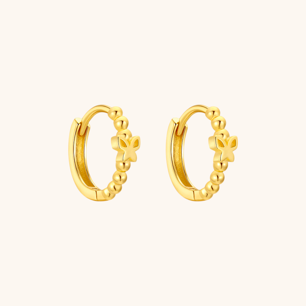 Close-up of gold butterfly hoop earrings on white background, featuring a delicate beaded design.