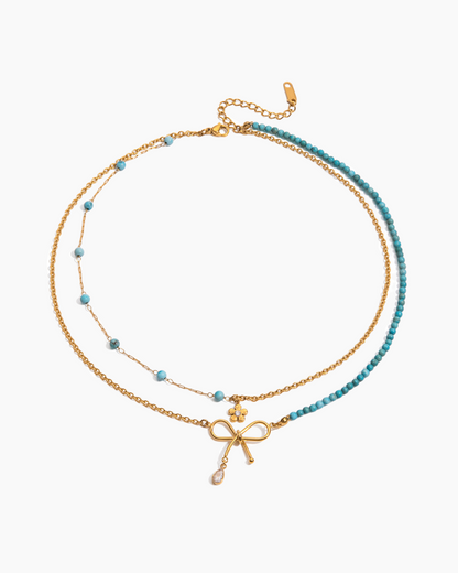 Two layered necklaces with bow and cross pendants on a white background