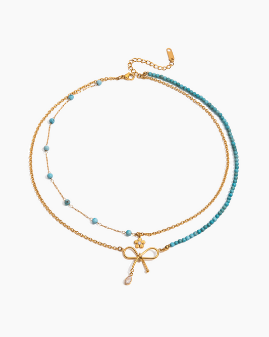Two layered necklaces with bow and cross pendants on a white background