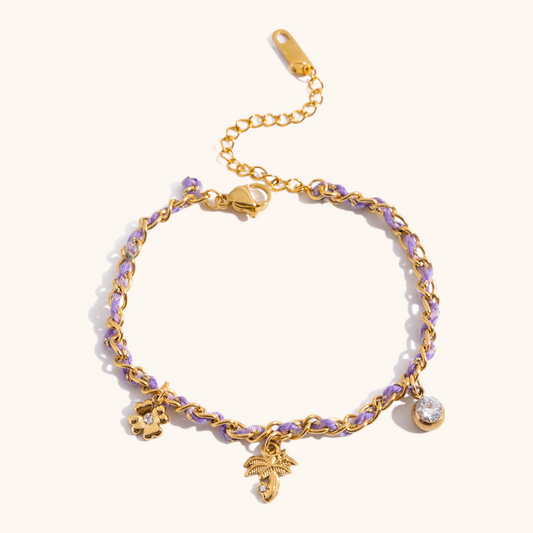Close-up of lilac-thread gold chain bracelet with palm, flower, and crystal charms on light textured background