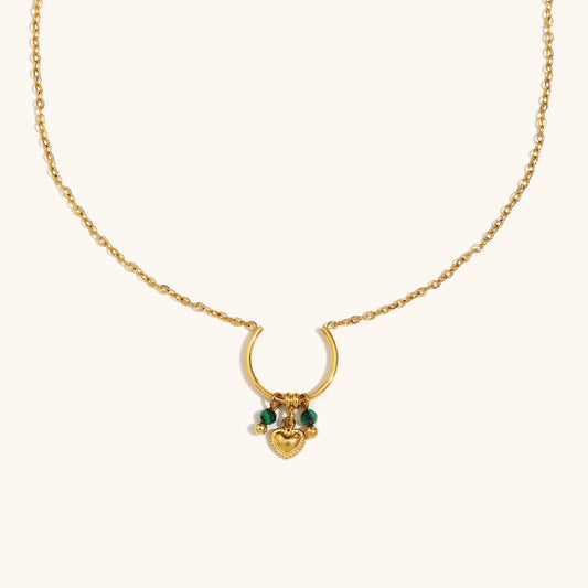 Gold crescent necklace with mini green beads and heart pendant on cream background.
