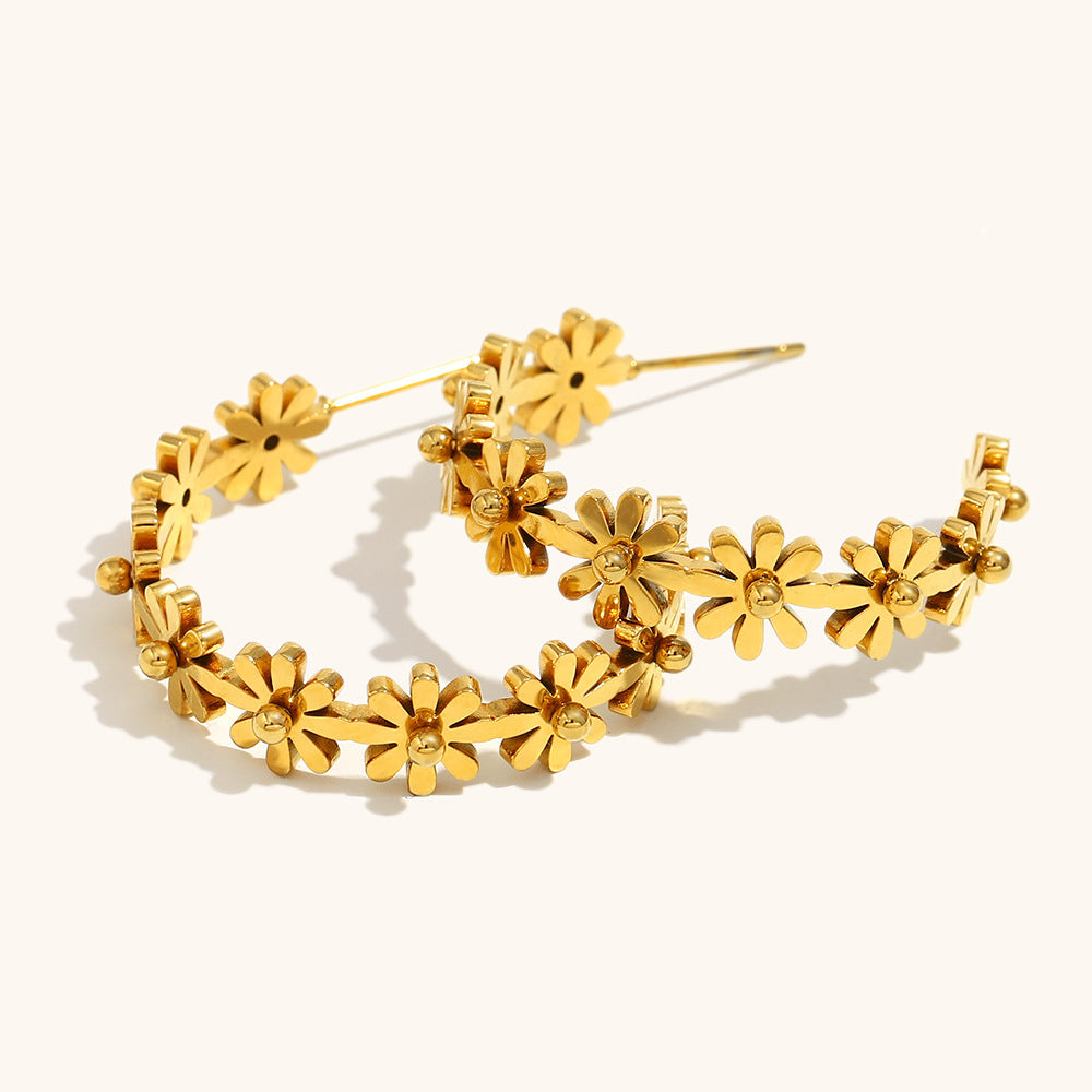 gold-plated daisy hoop earrings styled next to a ceramic object under natural light, casting floral shadows