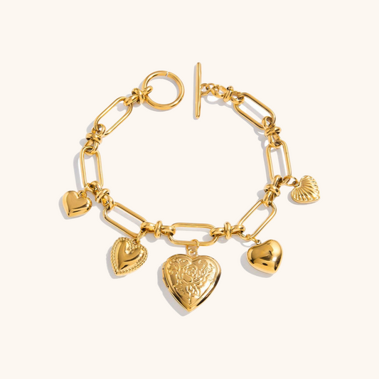 Flat lay of chunky gold bracelets with heart and flower pendants