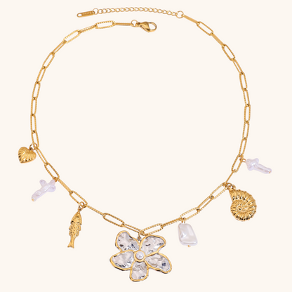 Gold chain necklace with a large hammered flower pendant, shell, and pearl charms on white background
