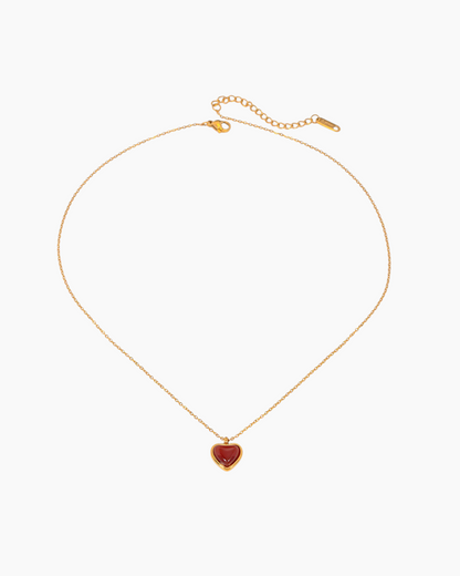 Gold necklace with a heart-shaped red pendant on a white background