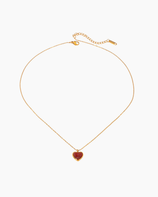 Gold necklace with a heart-shaped red pendant on a white background